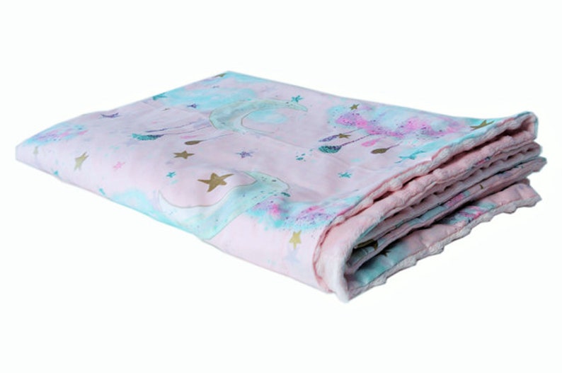 May include: A pink and blue baby blanket featuring a unicorn and stars design. The blanket is folded and has a soft, plush feel.
