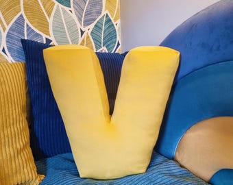 Może przedstawiać: Żółta poduszka w kształcie litery V na niebieskiej sofie z innymi poduszkami. Sofa ma niebieską, żółtą i brązową tkaninę.