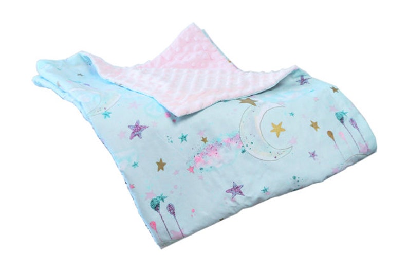 May include: A soft, blue and pink baby blanket with a moon and stars pattern. One side is a soft, plush fabric and the other side is a smooth cotton fabric.