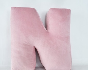 Könnte beinhalten: Ein großes, plüschiges N-Kissen in zartem Rosa. Das Kissen ist aus einem samtigen Stoff mit einer dezenten Textur.
