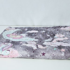 May include: A soft grey and pink baby blanket with a unicorn and moon design. The blanket features a repeating pattern of unicorns, moons, and stars.