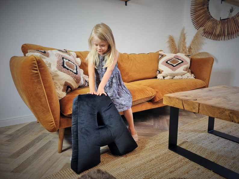 Decorative pillow in the shape of the letter A in black. The pillow can lie on a child's bed, on the floor, serve as a seat, decorating the room and referring to the name starting with the letter A. The pillow is large, soft, made of velvet.