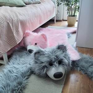 May include: A gray and pink faux fur rug with a gray wolf and a pink bear plush toy. The rug is on a wooden floor.