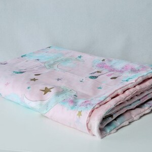 May include: A pink and blue baby blanket featuring a unicorn and star design. The blanket is folded and has a soft, plush texture.