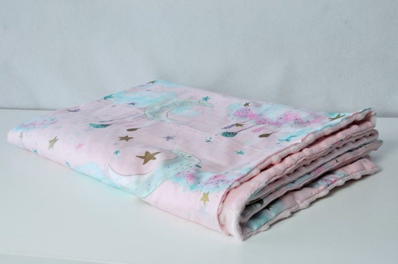 May include: A pink and blue baby blanket featuring a unicorn and star design. The blanket is folded and has a soft, plush texture.