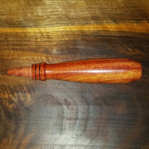 May include: A wooden tool with a red and brown finish. The tool has a rounded handle and a pointed end.