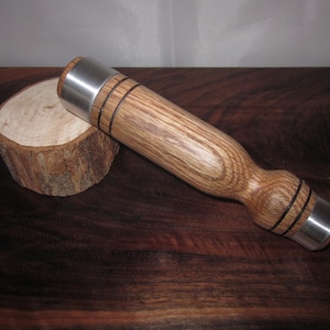 May include: A wooden mallet with a brown oak handle and silver metal ends. The mallet has two black bands around the handle.