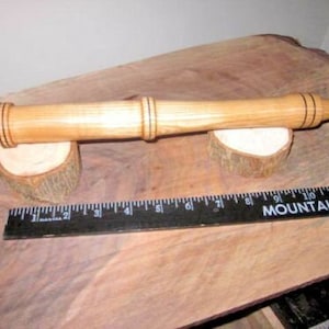 Puede incluir: Una varilla de madera con anillos negros en cada extremo. La varilla está apoyada en dos pequeños bloques de madera. Una regla negra con marcas blancas y el texto "Mountain Valley" está en primer plano.