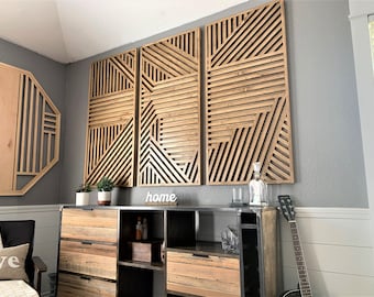 May include: Three wooden wall panels with a geometric pattern of horizontal and diagonal lines. The panels are arranged in a row and are mounted on a gray wall. The panels are made of light brown wood and have a natural finish. The word "home" is written in white letters on a shelf below the panels.
