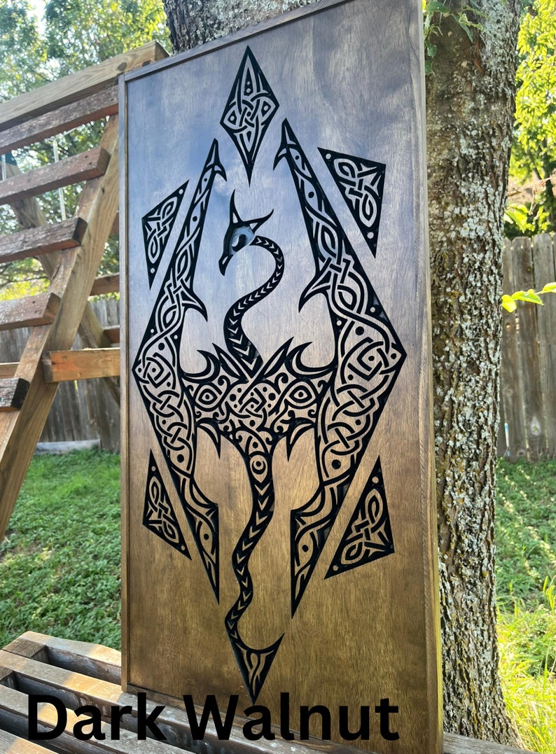 K&ouml;nnte beinhalten: Eine Wandplakette aus dunklem Walnussholz mit einem schwarzen Drachenmotiv. Der Drache ist in einem keltischen Knotenmuster dargestellt. Die Plakette ist ein dekoratives St&uuml;ck f&uuml;r ein Zuhause oder B&uuml;ro.