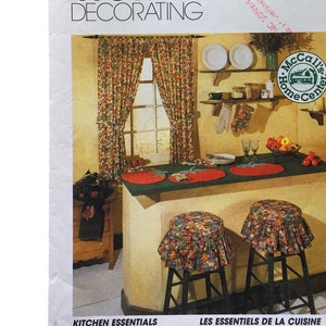 Op de afbeelding: Een McCall's Home Decorating-patroon voor keuken essentials. Het patroon toont een landelijke keuken met een aanrecht, twee barkrukken en een raam met gordijnen. Het patroonnummer is 8088. De tekst op het patroon luidt "Kitchen Essentials" en "Les Essentiels de la Cuisine".