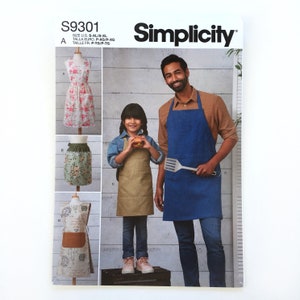 May include: A sewing pattern for three aprons, one with a floral print, one with a green and floral print, and one with a brown and white print. The pattern is for sizes S-XL and is from Simplicity.