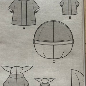 May include: A sewing pattern for a plush toy, featuring a character from the Star Wars series, The Mandalorian. The pattern includes instructions for making the character's body, head, and a floating pod.