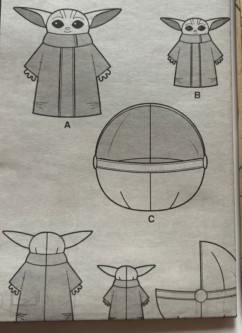 May include: A sewing pattern for a plush toy, featuring a character from the Star Wars series, The Mandalorian. The pattern includes instructions for making the character's body, head, and a floating pod.