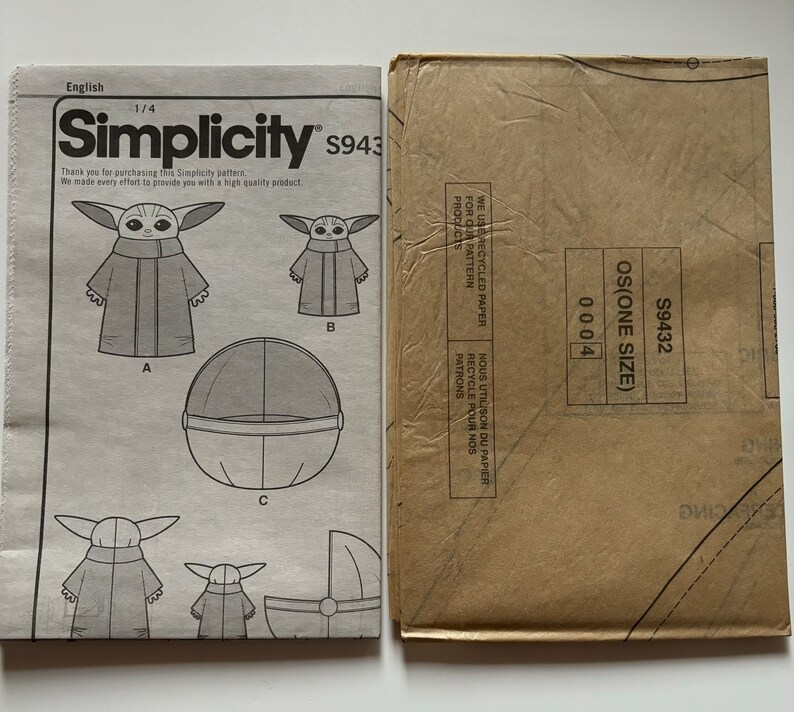 May include: A Simplicity sewing pattern for a baby costume. The pattern includes instructions for making a hooded robe, a floating pod, and a carrying cradle. The pattern number is S9432 and the size is OS (One Size).