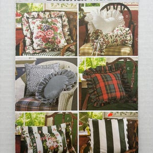 May include: A Butterick 6097 Waverly sewing pattern envelope featuring illustrations of various decorative pillows. Designs include floral prints, a heart-shaped pillow, a bolster pillow, a red and green plaid pillow, and striped pillows with ruffles.
