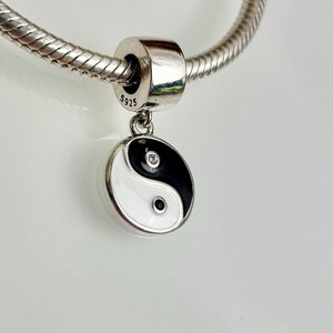 Könnte beinhalten: Ein silberner Anhänger mit einem schwarzen und weißen Yin-Yang-Symbol mit zwei kleinen, klaren Steinen. Der Anhänger ist an einer silbernen Kette befestigt.