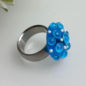 May include: A silver ring with a large blue and white glass cabochon. The cabochon is covered in small white dots and has a textured surface.
