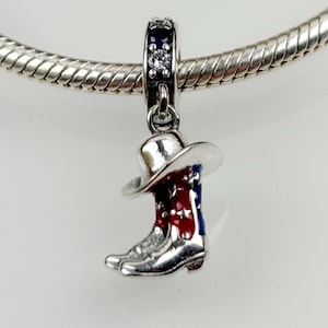 May include: Silver charm with a cowboy boot and hat design. The boot is red, white, and blue with stars. The charm has a clear crystal on the top.
