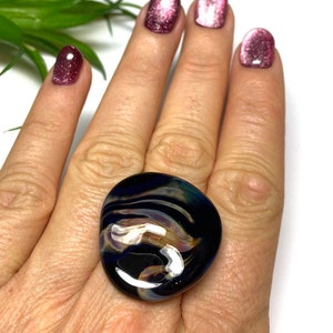 May include: A large, abstract, black, blue, and white glass ring. The ring has a swirling, marbled pattern.
