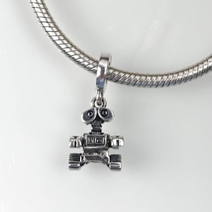 Peut inclure: Un charm argenté représentant un robot. Le robot a de grands yeux ronds, un corps rectangulaire et des chenilles. Il est suspendu à une chaîne argentée, parfait pour un bracelet.