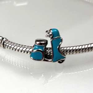 Könnte beinhalten: Ein silberner Charm mit einem türkisfarbenen Roller-Design. Der Roller hat ein detailliertes Aussehen mit Sitz, Lenker und einem vorderen Bereich. Der Charm ist an einem silbernen Armband befestigt.