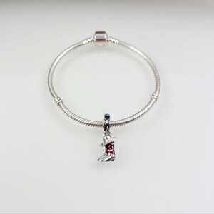 Pu&ograve; includere: Un braccialetto con ciondolo in argento con un ciondolo in argento a forma di stivale da cowboy con un design rosso, bianco e blu.