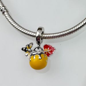 Op de afbeelding: Een zilveren armband met een honingpot bedel. De bedel is geel met een rood blad en een bij erop.