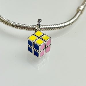 May include: A silver charm in the shape of a Rubik's Cube with yellow, pink, and blue squares.