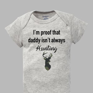 May include: A gray baby onesie with the text "I'm proof that daddy isn't always Hunting" and a camouflage deer silhouette.