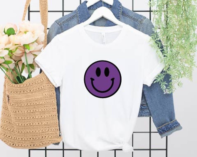 May include: White t-shirt with a purple smiley face graphic.