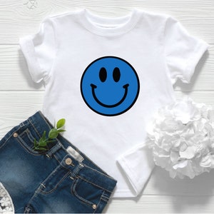 May include: White t-shirt with a blue smiley face graphic.