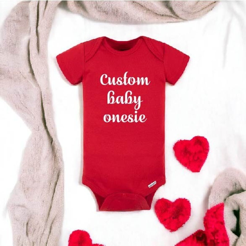 K&ouml;nnte beinhalten: Roter Baby-Strampler mit wei&szlig;em Text, der "Custom baby onesie" lautet. Der Strampler ist von roten, flauschigen Herzen auf wei&szlig;em Hintergrund umgeben.