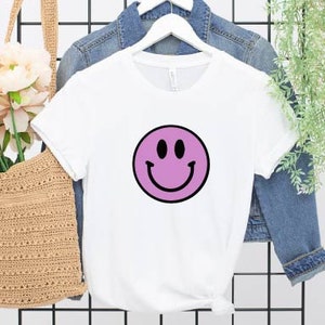 May include: White t-shirt with a purple smiley face graphic.