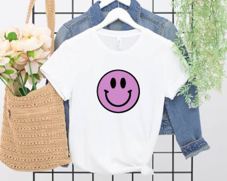 May include: White t-shirt with a purple smiley face graphic.