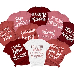 May include: Ten red and pink t-shirts with white text. The shirts have various wine-themed sayings, including "Sip Happens", "Hakuna Moscato", "Hit Me Baby One More Wine", "Wine Girl Wasted", "Stop and Smell the Rose", "Chardon Heyyy!", "Cabernet Then Slay", "I Make Pour Decisions", "Pour the Wine His Last Name is Mine!" and "When I Sip You Sip We Sip".