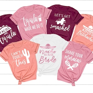 May include: Seven different t-shirts with various designs and text related to a bachelorette party. The shirts are in shades of pink, coral, and burgundy. The text on the shirts includes "Tacos and Tequila", "Tequila Made Me Do It", "Let's Get Smashed", "Adios Bitchachos", "Can't Touch This", "Nacho Average Bride", and "Shake Your Maracas".