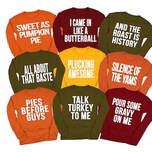 May include: A collection of nine long-sleeve crewneck sweatshirts in autumn colors including orange, maroon, olive green, and yellow. Each shirt features white text with phrases like Sweet as Pumpkin Pie, I Came in Like a Butterball, and Talk Turkey to Me.