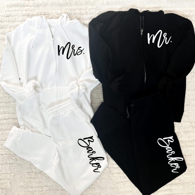 May include: A white and black matching set of zippered hoodies and sweatpants. The white hoodie has "Mrs." printed on the front and "Barker" printed on the leg of the sweatpants. The black hoodie has "Mr." printed on the front and "Barker" printed on the leg of the sweatpants.