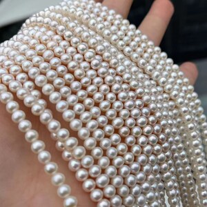 Peut inclure: Plusieurs rangées de perles blanches et rondes, tenues dans une main. Les perles sont de taille uniforme et présentent une surface brillante. L'image met en valeur le lustre naturel des perles, suggérant une bonne qualité. Idéal pour la création de bijoux.