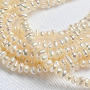 May include: A strand of off-white freshwater pearls, with a slightly irregular shape, arranged in a loose pile.