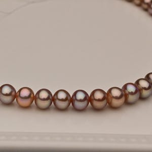 Peut inclure: Un collier de perles brunes irisées enfilées sur un cordon blanc. Les perles sont rondes et lisses, avec un léger chatoiement.