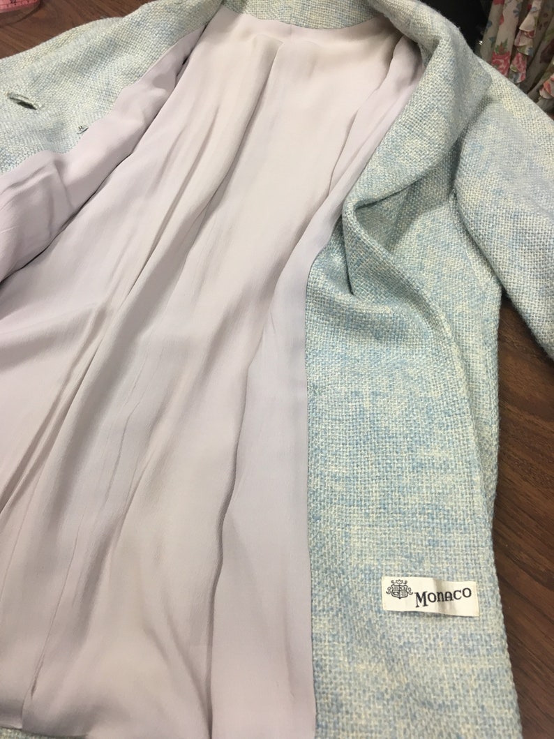 May include: A light blue blazer with a white and light blue patterned design. The blazer has a white lining and a label that says "Monaco".