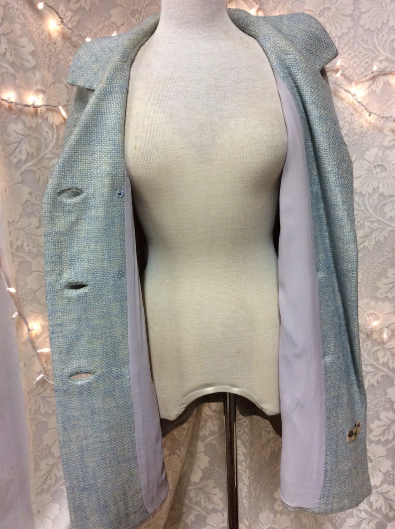 May include: A light blue blazer with a textured weave and a light gray lining. The blazer has a single button closure and two pockets.