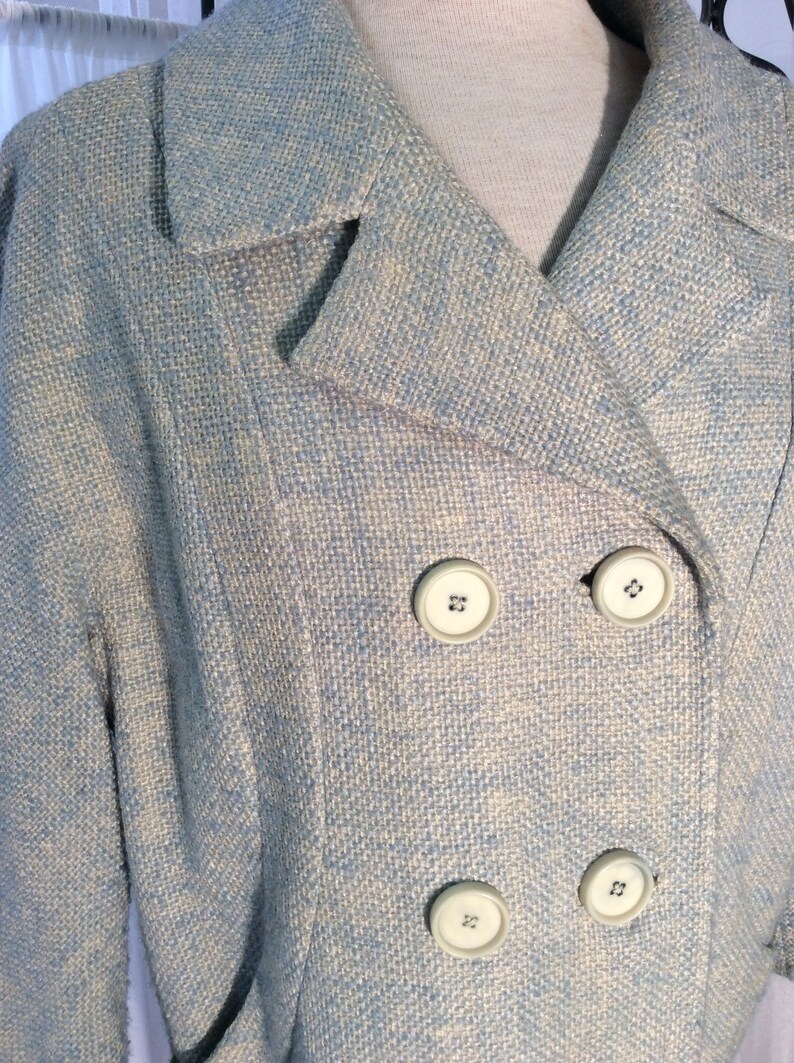 May include: A light blue blazer with a white and light blue patterned design. The blazer has a double breasted closure with four white buttons.