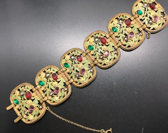May include: A gold-tone bracelet with a floral design and colorful rhinestones. The bracelet is made of metal and has a chain closure.