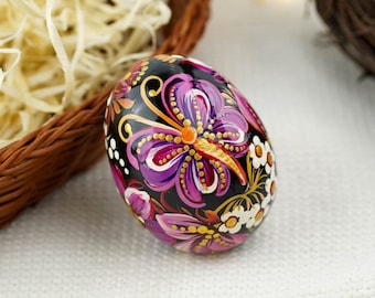 May include: A hand-painted Easter egg with a black background and a purple butterfly design. The butterfly has gold accents and white flowers surround it.