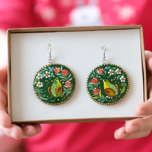 May include: A pair of green painted wooden earrings with a bird and floral design. The earrings are in a small box.