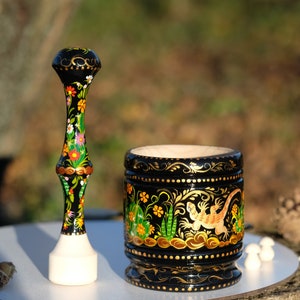 Puede incluir: Un mortero y un pilón de madera negra con intrincados diseños florales y de lagartos pintados en oro, verde, naranja y blanco.