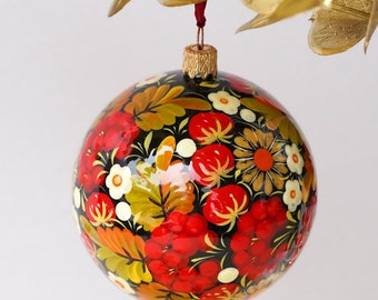 May include: A round, black Christmas bauble with a red, white and green floral design. The bauble is hand-painted with a glossy finish.